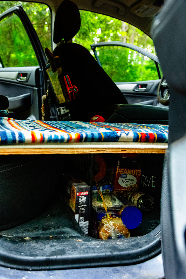 The plywood sleeping platform and blanket in the back of the car
